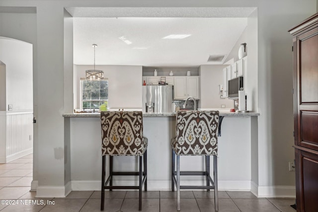 kitchen featuring light stone counters, appliances with stainless steel finishes, white cabinetry, a kitchen bar, and decorative light fixtures