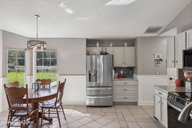 kitchen with decorative backsplash, light stone counters, light tile patterned floors, stainless steel appliances, and decorative light fixtures