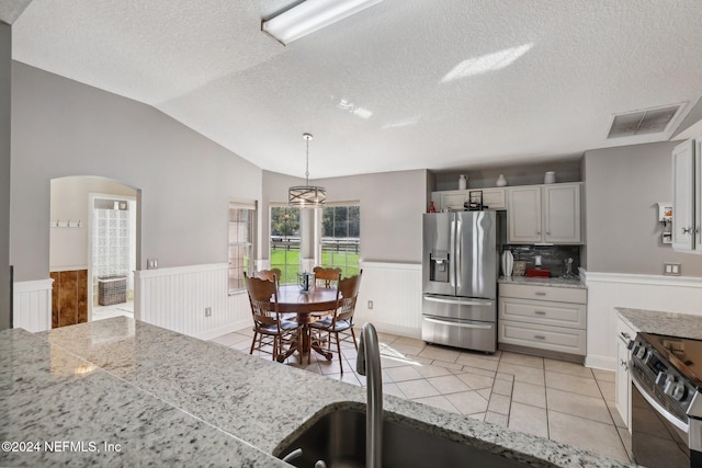 kitchen featuring a textured ceiling, stainless steel appliances, lofted ceiling, decorative light fixtures, and light tile patterned floors