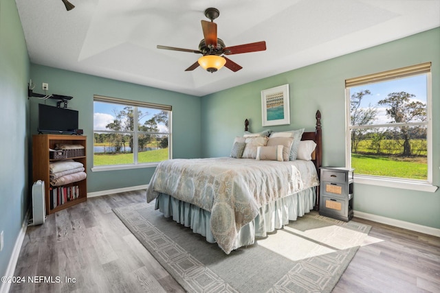 bedroom with a tray ceiling, wood-type flooring, and ceiling fan