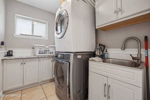 clothes washing area with sink, stacked washer and dryer, light tile patterned floors, and cabinets