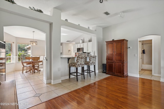 kitchen featuring kitchen peninsula, vaulted ceiling, pendant lighting, white cabinets, and light hardwood / wood-style flooring