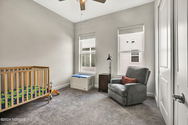 carpeted bedroom featuring a nursery area, ceiling fan, and baseboards