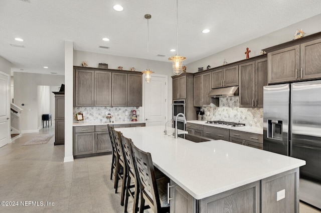 kitchen featuring hanging light fixtures, dark brown cabinets, a center island with sink, sink, and appliances with stainless steel finishes