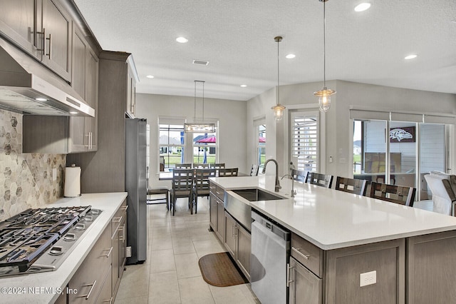 kitchen with appliances with stainless steel finishes, sink, light tile patterned flooring, decorative light fixtures, and a kitchen island with sink