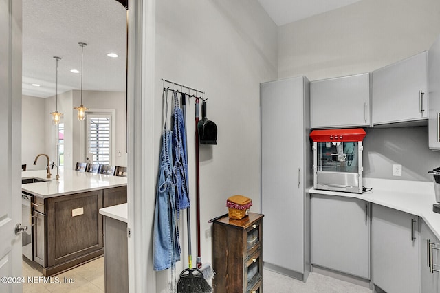 kitchen featuring light countertops, decorative light fixtures, a center island with sink, light tile patterned floors, and a sink