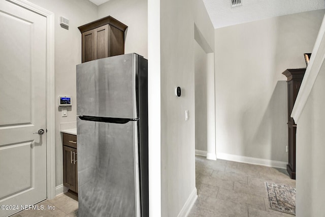 kitchen featuring dark brown cabinets, a textured ceiling, and stainless steel refrigerator