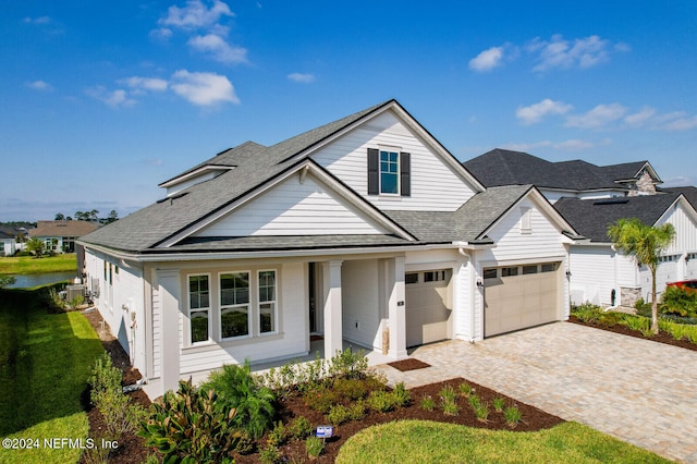 view of front of house featuring decorative driveway, an attached garage, and roof with shingles