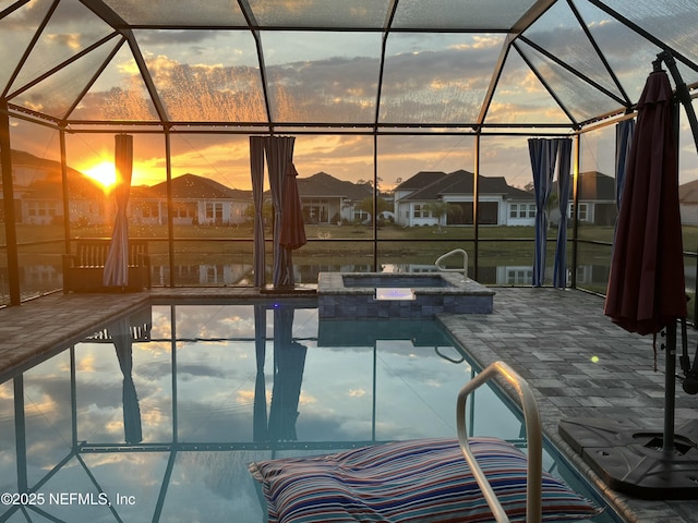 pool at dusk with a pool with connected hot tub, glass enclosure, a patio, and a residential view