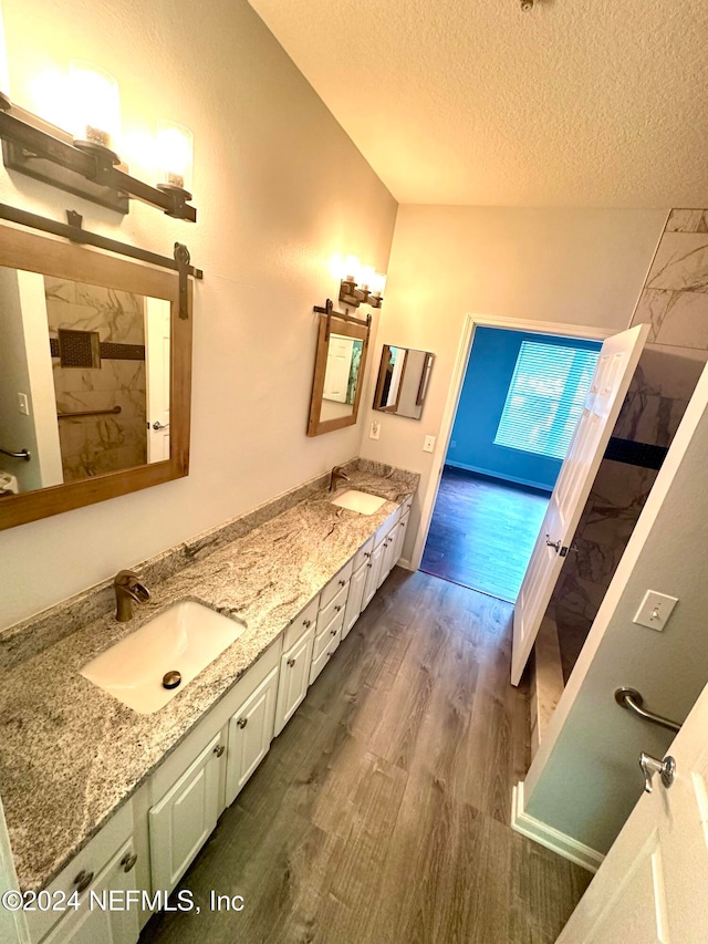 bathroom with vanity, hardwood / wood-style flooring, a textured ceiling, and lofted ceiling