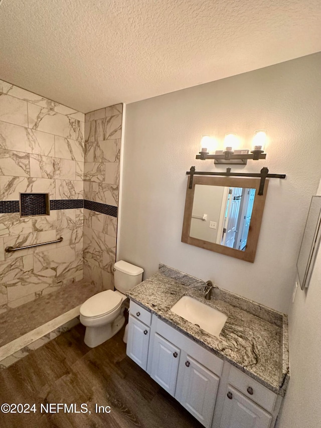 bathroom with tiled shower, toilet, hardwood / wood-style floors, vanity, and a textured ceiling