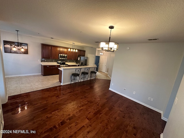 kitchen with an island with sink, appliances with stainless steel finishes, a breakfast bar area, light wood-type flooring, and decorative light fixtures