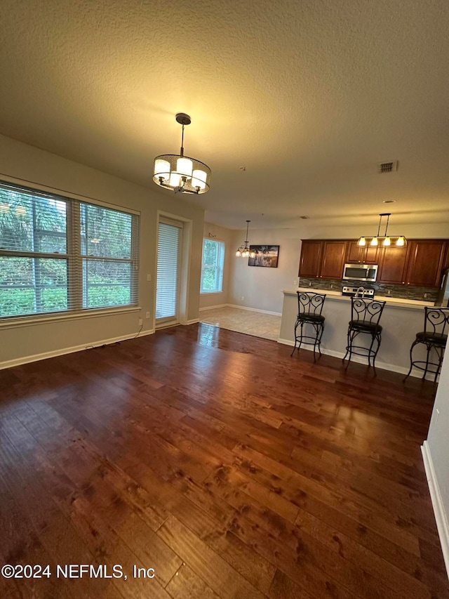 unfurnished living room featuring dark wood-type flooring, a textured ceiling, and an inviting chandelier