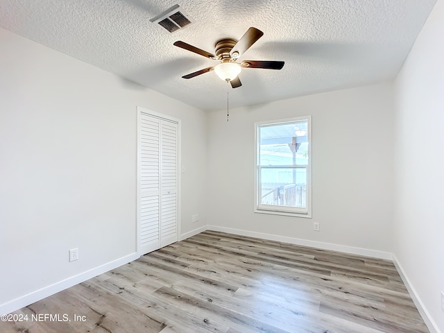 unfurnished bedroom featuring a closet, a textured ceiling, light wood-type flooring, and ceiling fan