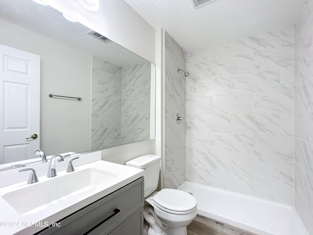 bathroom featuring vanity, a tile shower, a textured ceiling, and toilet