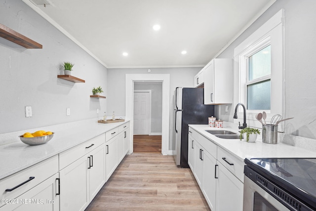 kitchen featuring stove, white cabinetry, stainless steel refrigerator, and sink