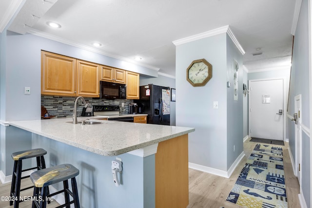 kitchen with backsplash, light stone counters, sink, black appliances, and a breakfast bar area