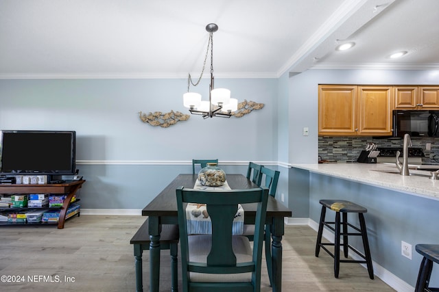 dining space with sink, light hardwood / wood-style flooring, crown molding, and a notable chandelier