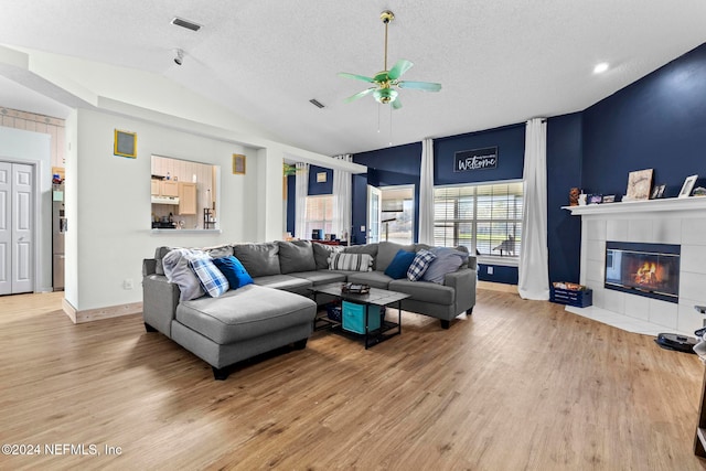 living room with ceiling fan, a textured ceiling, hardwood / wood-style flooring, vaulted ceiling, and a tile fireplace