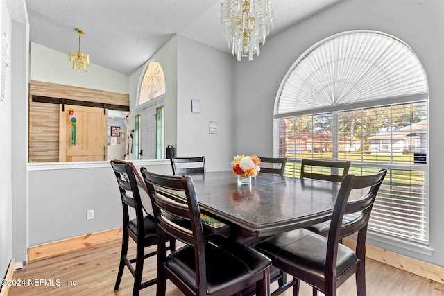 dining space featuring hardwood / wood-style floors, a textured ceiling, a barn door, vaulted ceiling, and a notable chandelier