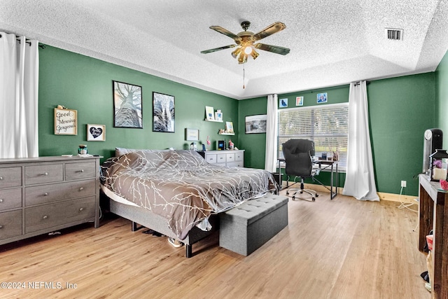 bedroom featuring a raised ceiling, light hardwood / wood-style flooring, a textured ceiling, and ceiling fan