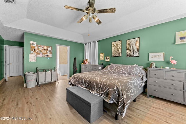 bedroom with light hardwood / wood-style floors, a textured ceiling, a tray ceiling, and ceiling fan