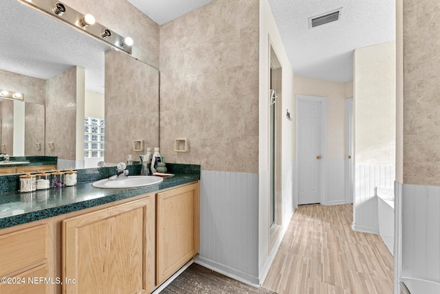 bathroom featuring vanity, hardwood / wood-style floors, plus walk in shower, and a textured ceiling