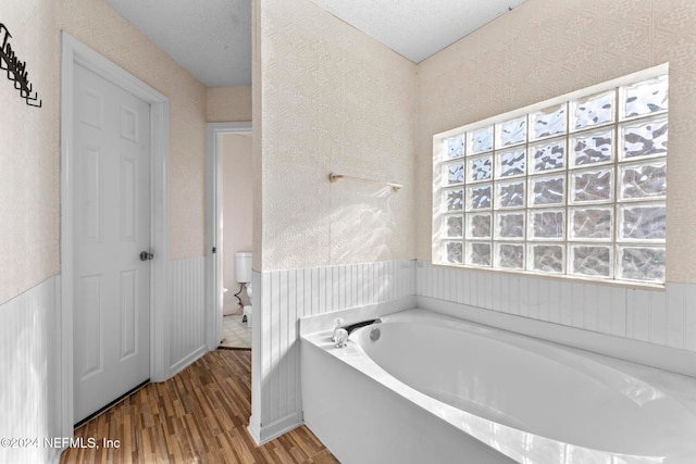 bathroom featuring plenty of natural light, a textured ceiling, wood-type flooring, and a washtub