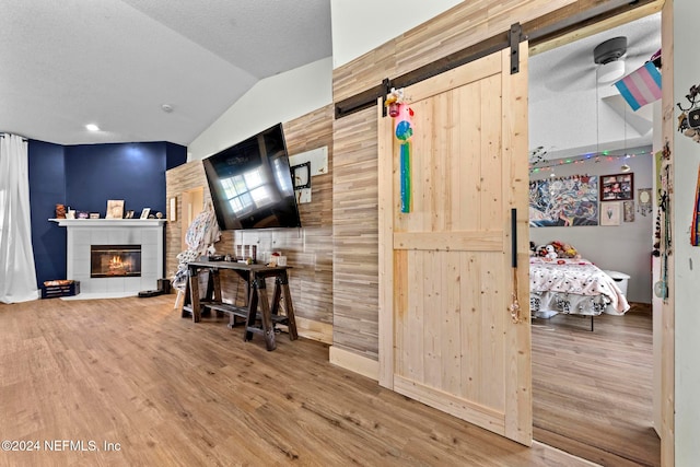 interior space with lofted ceiling, wood walls, a barn door, and wood-type flooring