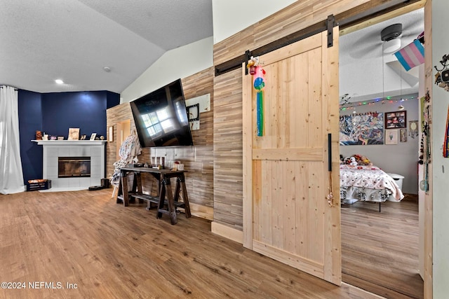 interior space with lofted ceiling, a barn door, hardwood / wood-style flooring, and wood walls