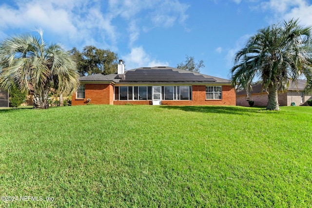 back of property featuring a lawn and solar panels