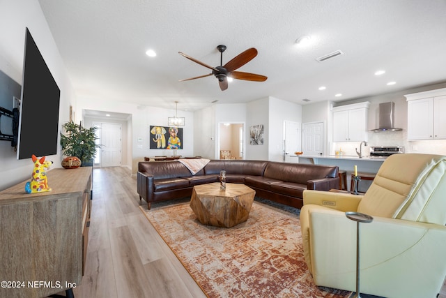 living room featuring ceiling fan, a textured ceiling, and light wood-type flooring