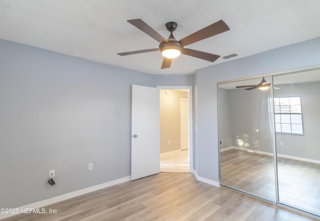 unfurnished bedroom featuring ceiling fan, light wood-type flooring, a textured ceiling, and a closet