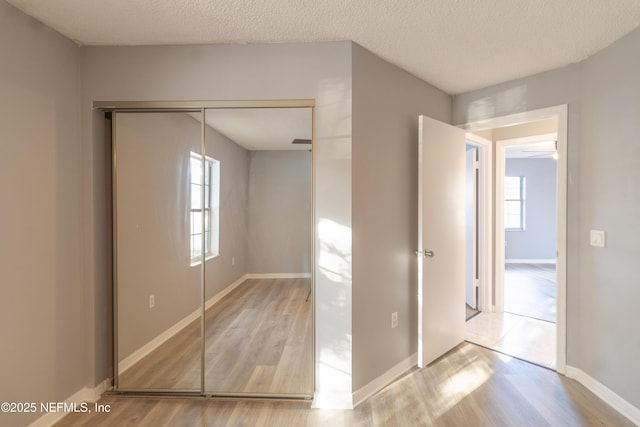 unfurnished bedroom featuring light hardwood / wood-style floors, a textured ceiling, and a closet