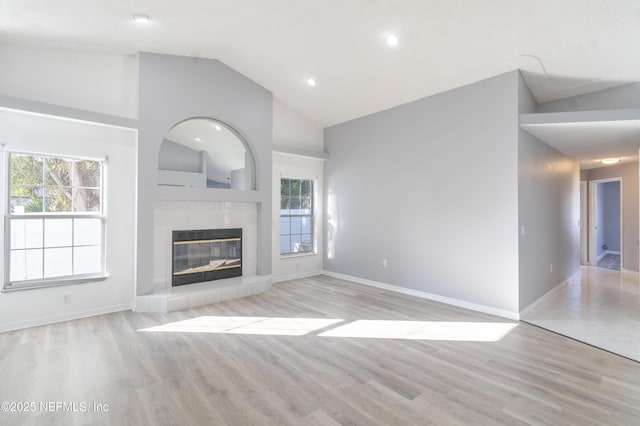 unfurnished living room featuring a fireplace, light wood-type flooring, high vaulted ceiling, and plenty of natural light