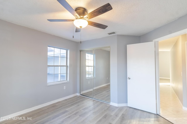 unfurnished bedroom with ceiling fan, a closet, a textured ceiling, and light wood-type flooring