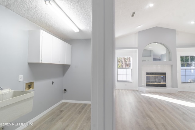 laundry room featuring cabinets, a tile fireplace, light hardwood / wood-style flooring, a textured ceiling, and hookup for an electric dryer