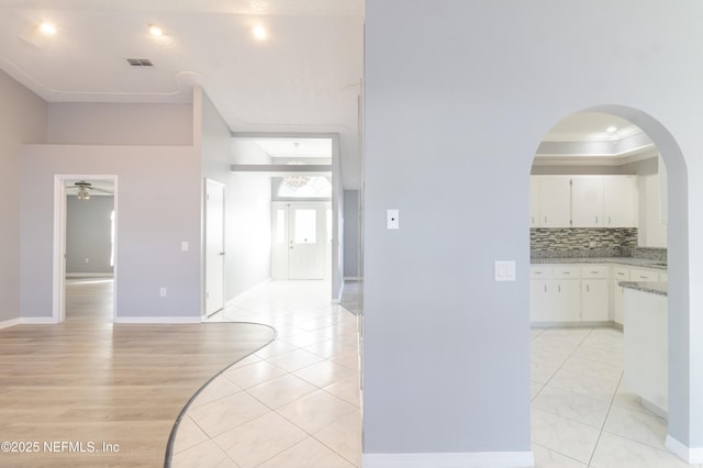 hallway featuring a raised ceiling, crown molding, and light tile patterned floors