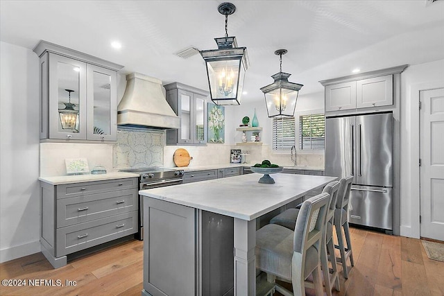 kitchen featuring custom exhaust hood, stainless steel appliances, pendant lighting, and light hardwood / wood-style floors