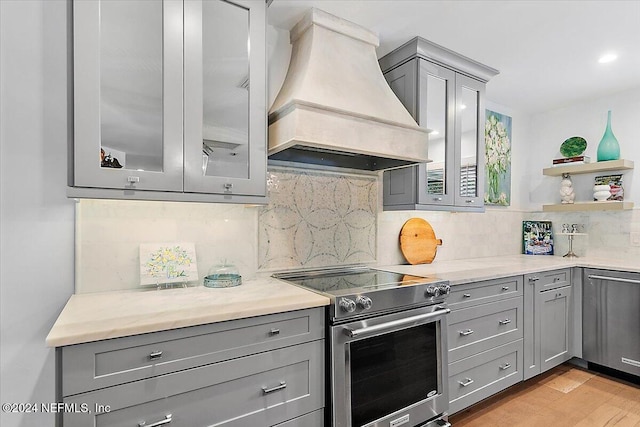 kitchen featuring decorative backsplash, gray cabinets, light hardwood / wood-style flooring, custom range hood, and stainless steel range