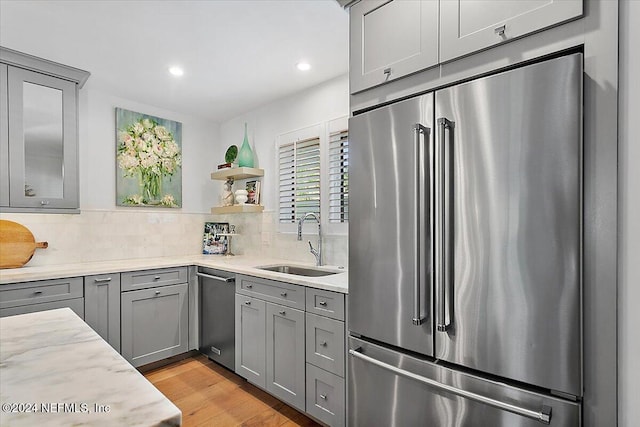 kitchen with backsplash, sink, light wood-type flooring, appliances with stainless steel finishes, and light stone counters