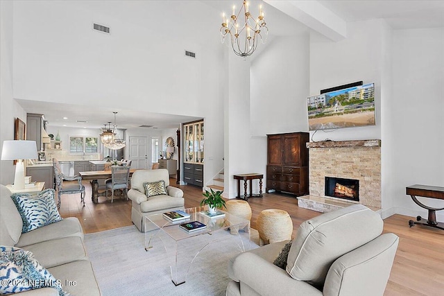 living room with light hardwood / wood-style floors, a stone fireplace, beamed ceiling, a chandelier, and a towering ceiling