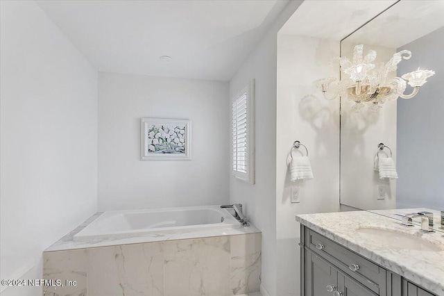 bathroom with vanity, a chandelier, and tiled tub