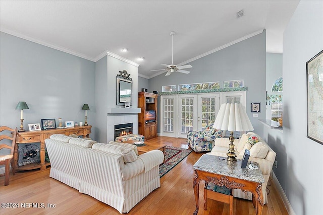 living room with light hardwood / wood-style floors, a tiled fireplace, french doors, high vaulted ceiling, and crown molding