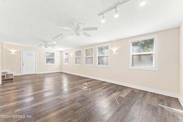 empty room featuring a textured ceiling, track lighting, dark hardwood / wood-style flooring, and plenty of natural light