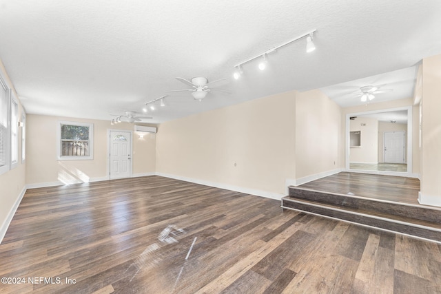 unfurnished room with a wall mounted air conditioner, a textured ceiling, rail lighting, ceiling fan, and dark hardwood / wood-style floors