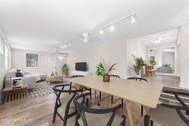 dining room with a wall unit AC, wood-type flooring, rail lighting, a textured ceiling, and ceiling fan