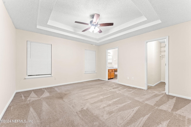 unfurnished bedroom with light carpet, ceiling fan, a spacious closet, a tray ceiling, and ensuite bathroom