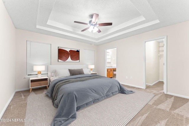 bedroom with ensuite bathroom, a raised ceiling, a textured ceiling, light carpet, and ceiling fan