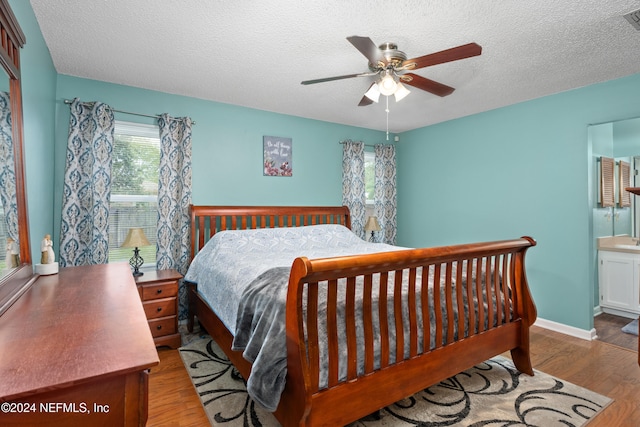 bedroom with light hardwood / wood-style floors, a textured ceiling, ensuite bathroom, and ceiling fan